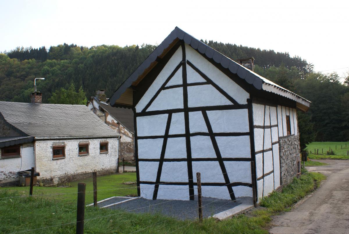 Petite maison à colombages (poutres et torchis blanc) avec ancienne pompe à eau à l’avant plan et un coq reflétant l’aspect champêtre de ce hameau de Challes.