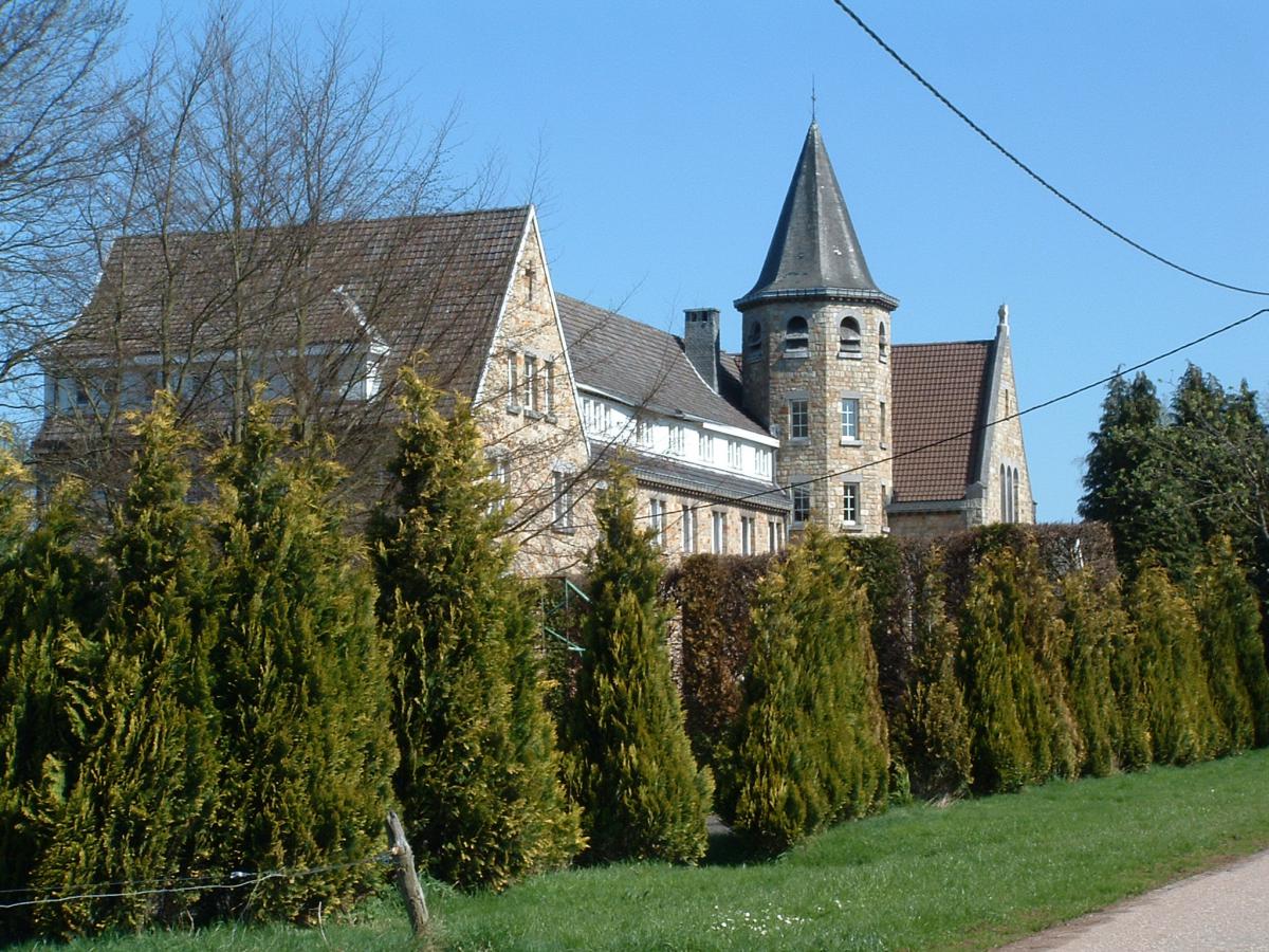 Vue sur une partie du monastère Saint-Rezmacle situé en pleine verdure à l’écart du village de Wavreumont ; bâtiment et église en pierres du pays.